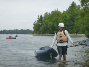 Photo of kid standing in the water bringing their blue inflatable kayak out of the water