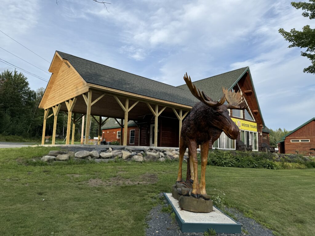 Outside view of Northeast Whitewater with a life size wooden moose on the lawn in front of the building that has the new pavilion addition attached to it.