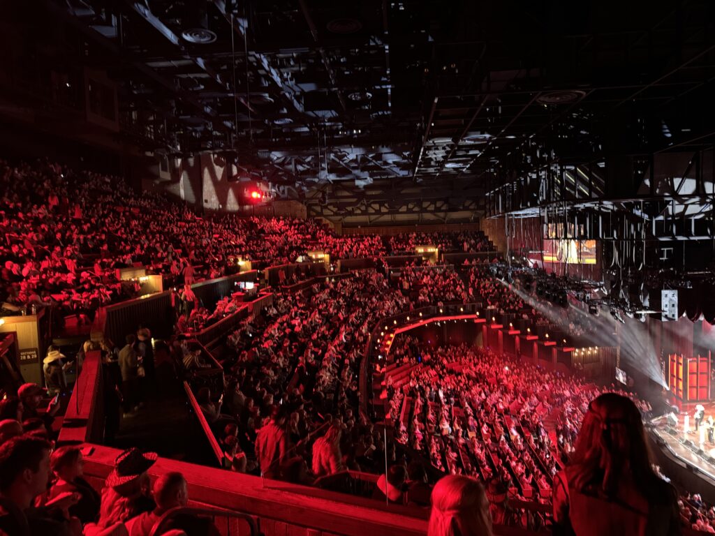 View of the center seating at the Grand Ole Opry, the lighting cast on the crowd is red.