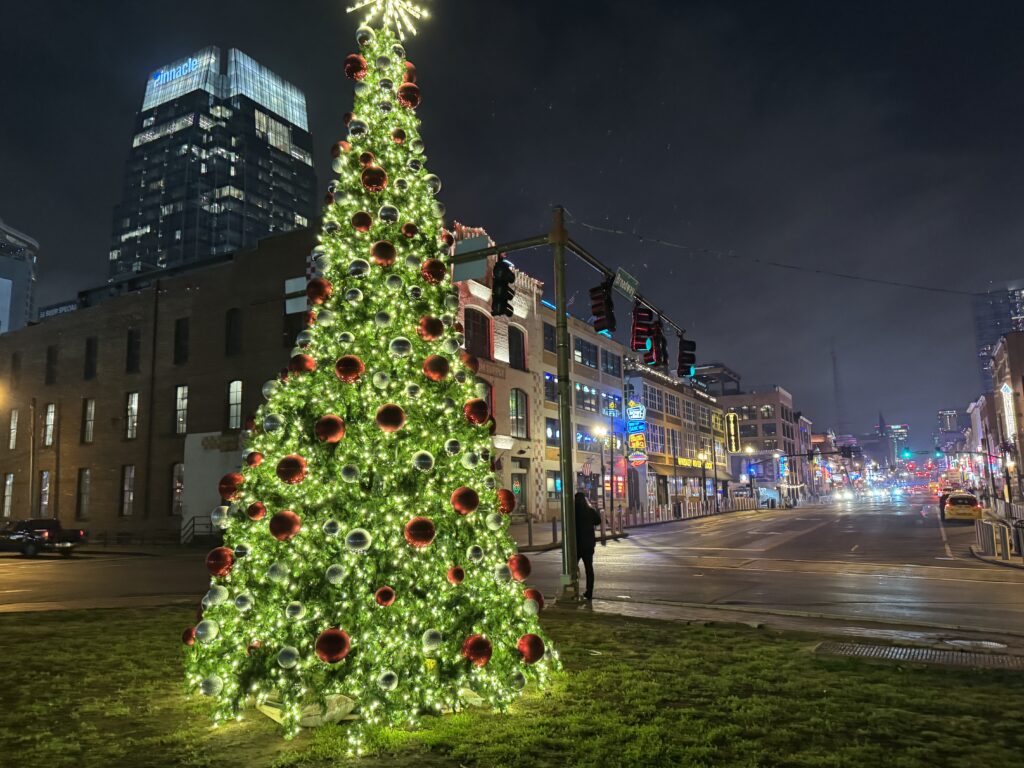 Christmas tree at night with yellow light and red bulbs in Nashville. You can see the Nashville strip in the background behind the tree.