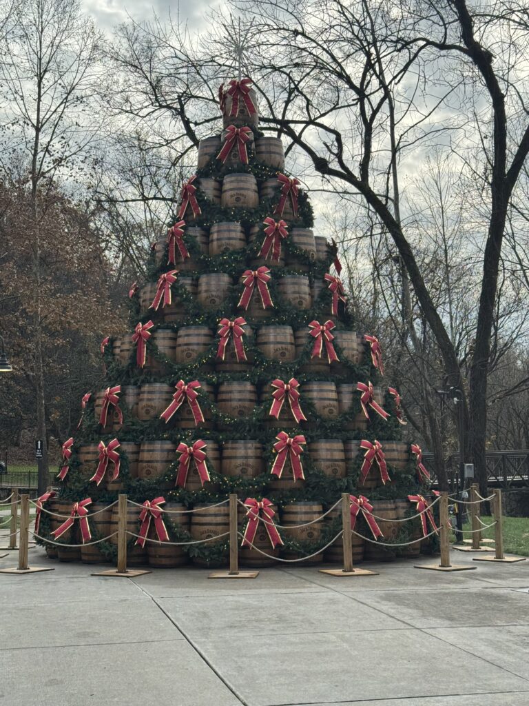 Very large Christmas tree made out of Jack Daniels bourbon barrels with green garland and red bows.