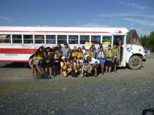 Group of campers wearing PFDs standing together in front of white bus