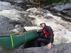 Man Sitting Next to a Canoe on a River